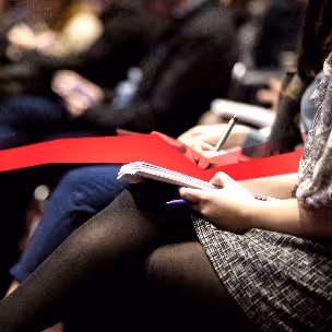 A woman holds a notepad on her lap and writes something down, a string of red data leads through the picture.