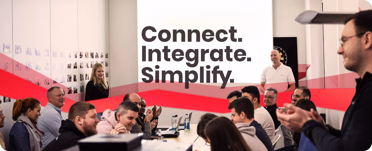 A group of people sit around a table and carry a sign that says Connect, Integrate, Simplify.