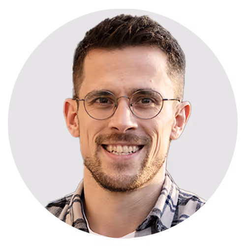Porträt eines lächelnden Mannes mit kurzen braunen Haaren, Bart, Brille und kariertem Hemd.