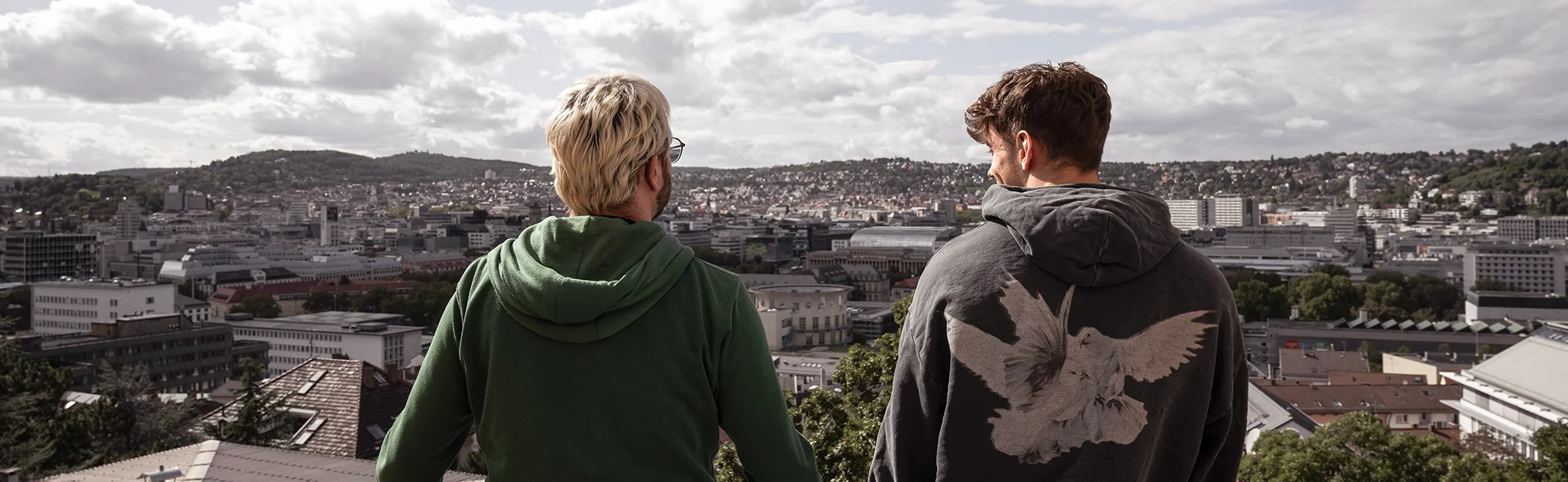 Zwei Männer von hinten sehen auf eine Großstadt mit bewölktem Himmel.