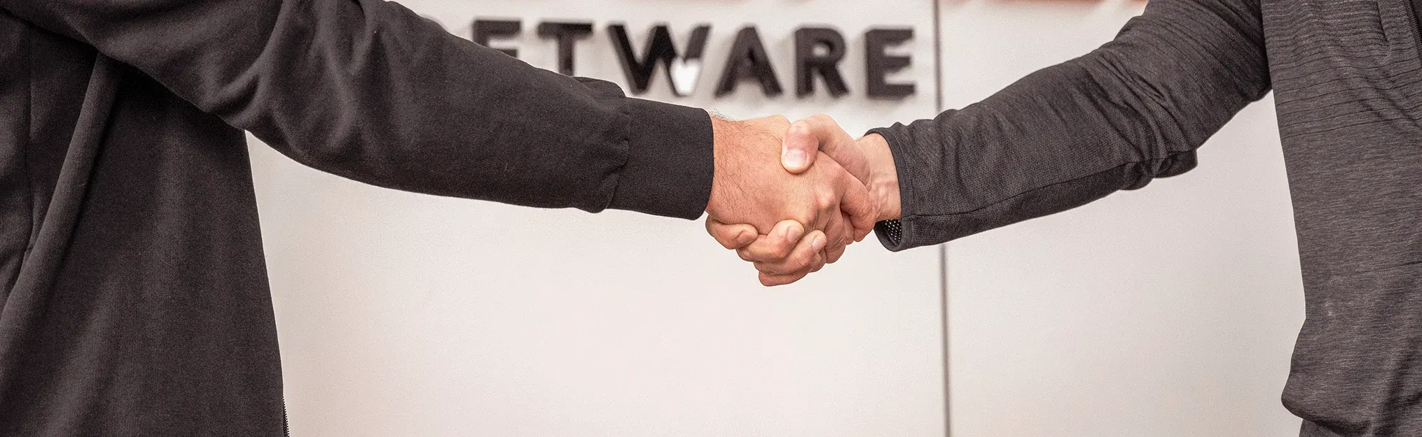 Zwei Personen geben sich vor einem Schild mit der Aufschrift "SOFTWARE" die Hand.