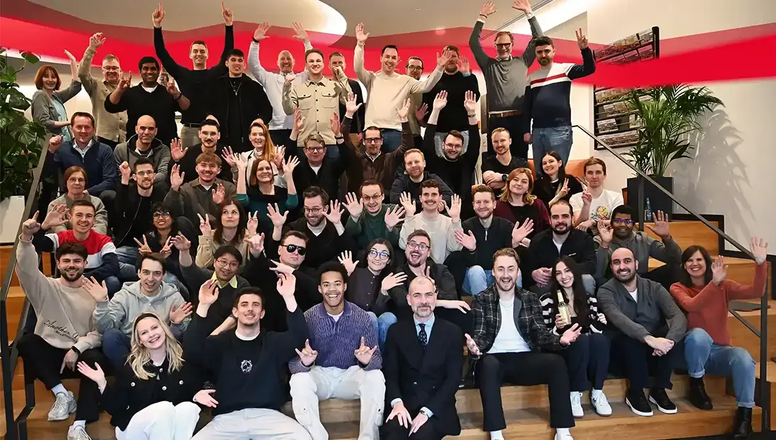 Große Gruppe von Menschen verschiedener Altersgruppen auf einer Treppe, die in die Kamera lächeln und winken.