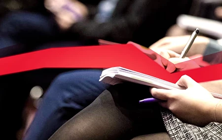 A woman is holding a notepad on her lap and writing something down; a red data stream runs across the image.