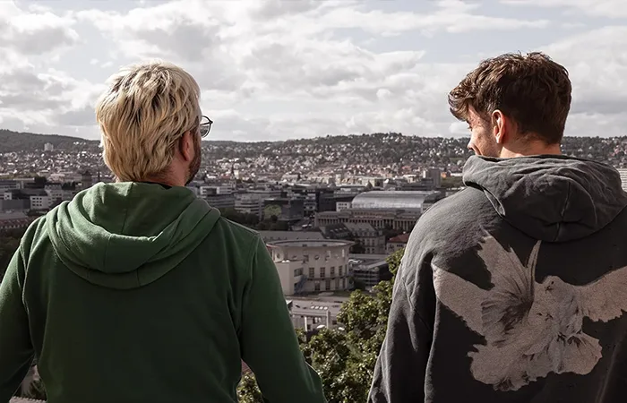 Two men are standing on a balcony, looking out over Stuttgart.