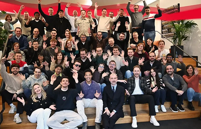 Große Gruppe von Menschen sitzt und steht auf Treppenstufen, lächelt und winkt zur Kamera.