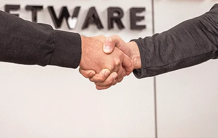 Zwei Personen geben sich vor einem Schild mit der Aufschrift "SOFTWARE" die Hand.