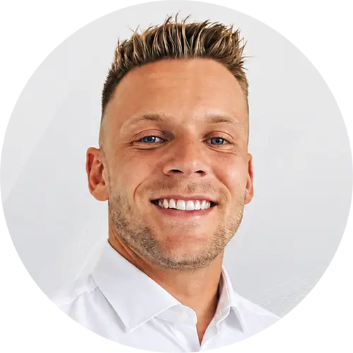 Portrait eines lächelnden Mannes mit kurzen blonden Haaren und weißem Hemd vor weißem Hintergrund.