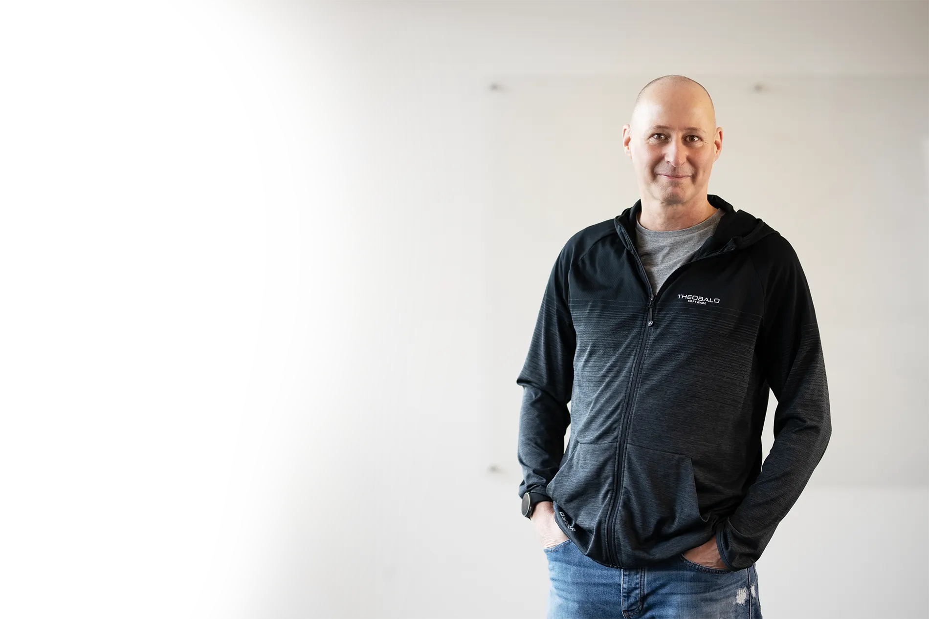 Mann in schwarzer Theobald Software Jacke und Jeans vor hellgrauem Hintergrund.