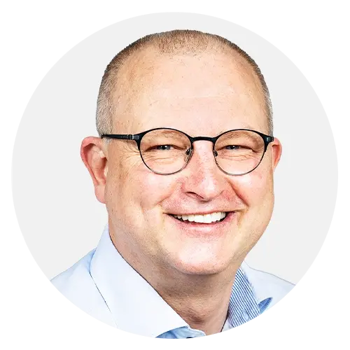Lachender Mann mit Brille und blauem Hemd vor weißem Hintergrund.
