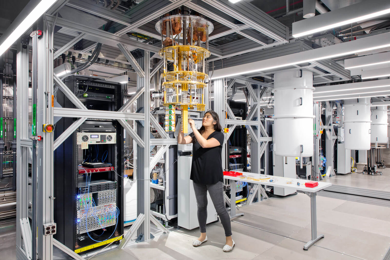 IBM’s Dr. Maika Takita works inside a quantum computing lab, interacting with a large cryogenic cooling system surrounded by server racks and research equipment. 
Image credit: Connie Zhou for IBM