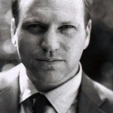 Black-and-white portrait of Gary Andrew Poole wearing a suit and tie, looking directly at the camera with a neutral expression. 