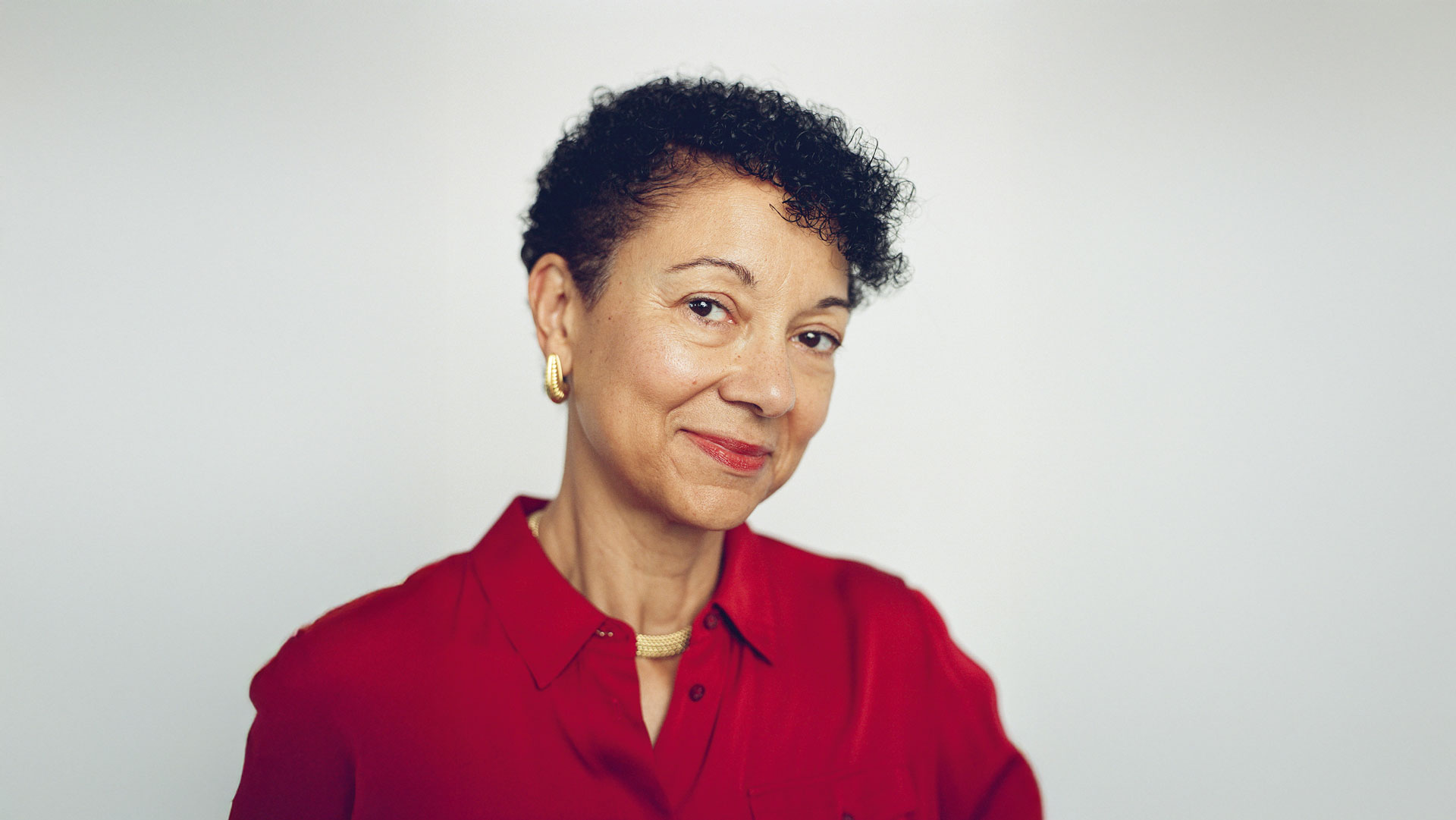 Portrait of Shellye Archambeau wearing a red shirt and gold jewelry, photographed by Ysa Pérez for Think:Act Magazine.
