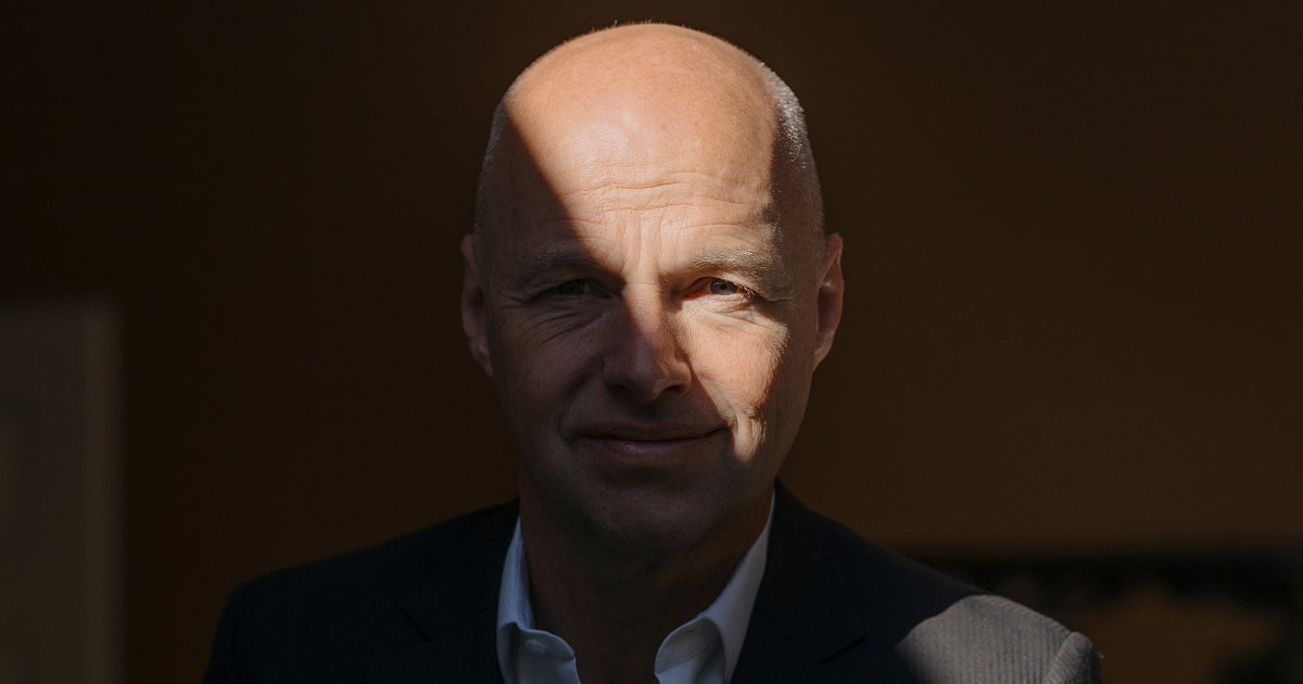 Portrait of Sebastian Thrun in a dark suit and white shirt, seated in dramatic lighting. A diagonal beam of light falls across his face against an otherwise dark background, highlighting his features while the rest of the scene remains in shadow.