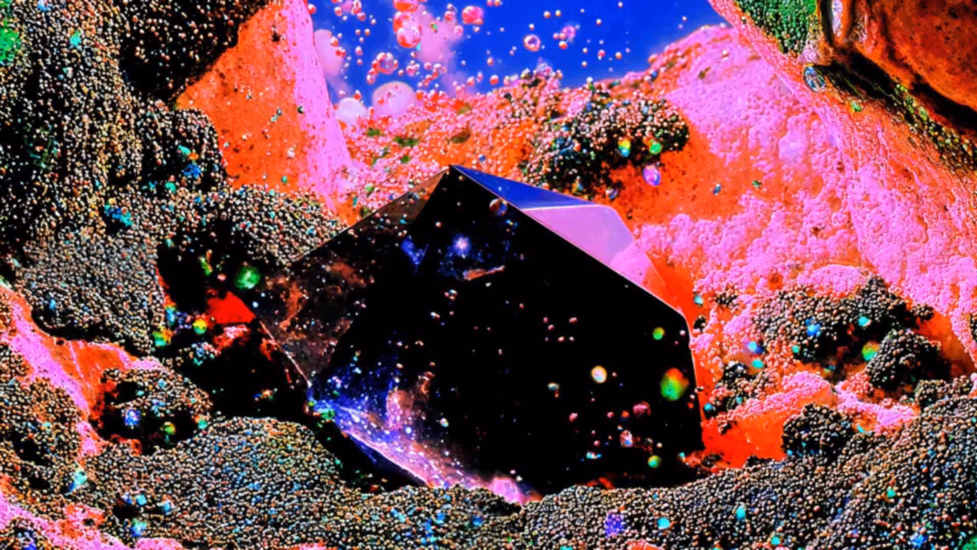 A smooth, dark geometric crystal rests within a vibrant, microscopic-style landscape of neon pink formations and dark, bead-like textures, with colorful floating orbs suspended against a bright blue background.