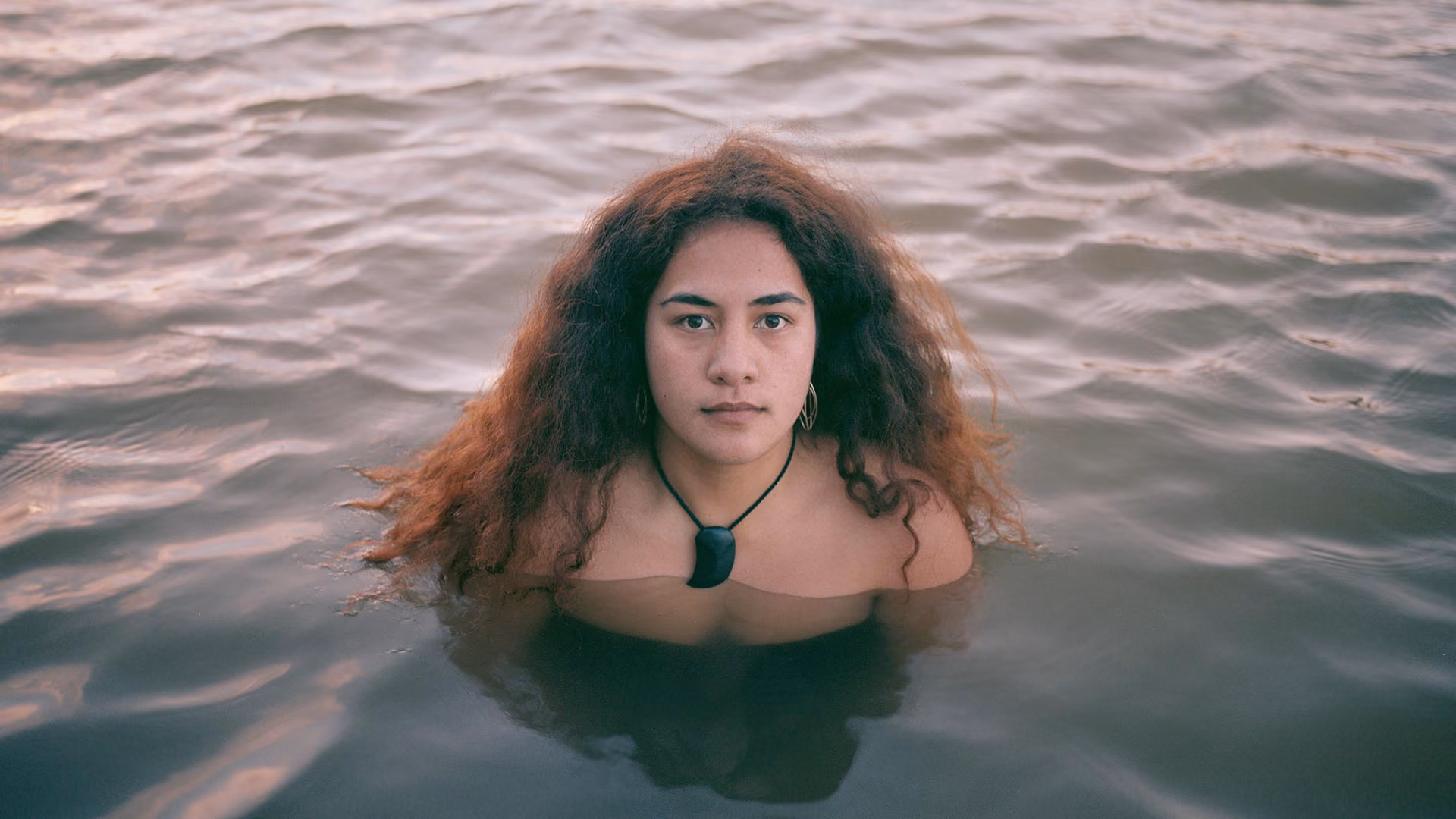 Eine Frau mit einem Pounamu-Anhänger steht brusttief im Wasser – Sinnbild für die kulturelle Bedeutung des Whanganui River.
