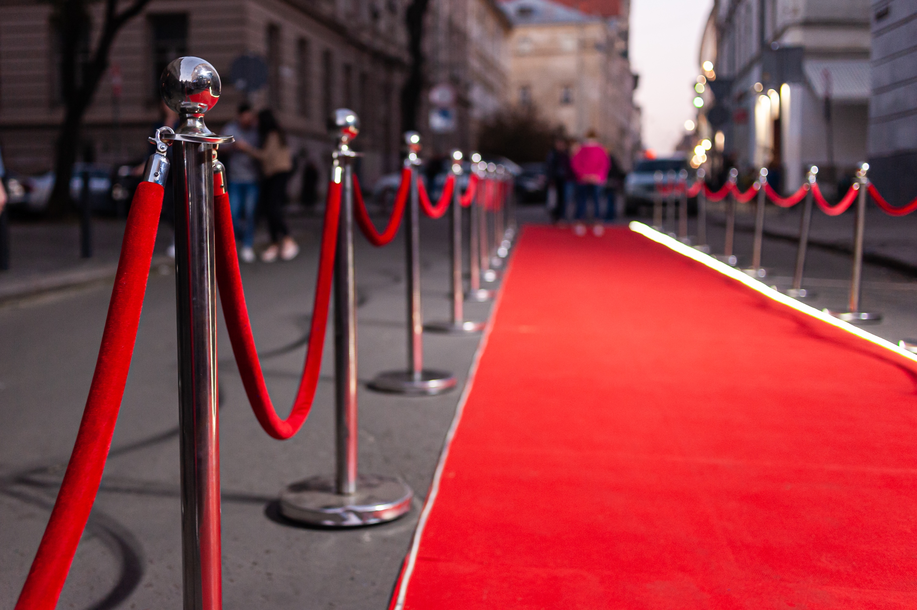 Red carpet with velvet ropes set up on a city street for an event.