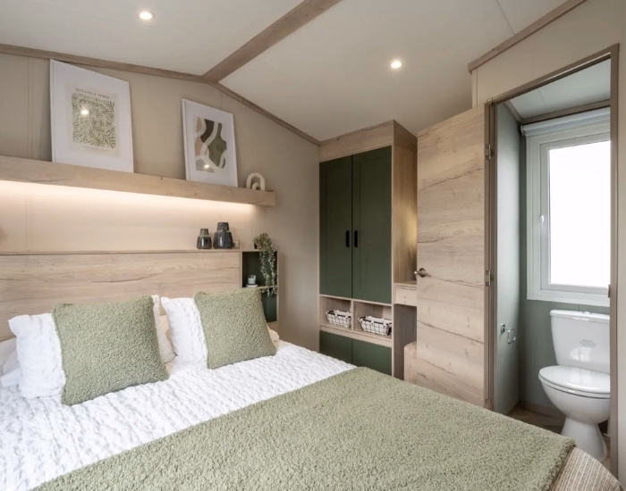 Ripley – Slaapkamer met tweepersoonsbed, groen hoofdbord, houten kasten en eigen toilet.