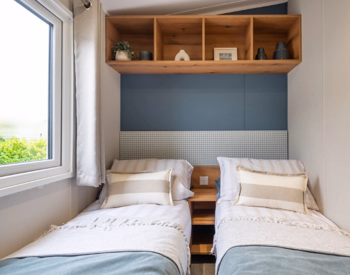 Ashberry – Tweepersoonsslaapkamer met blauw beddengoed, donker hoofdbord en raam.