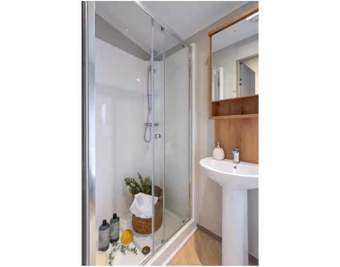 Ashberry – Badkamer met glazen douchecabine, witte wastafel en houten wandkast.
