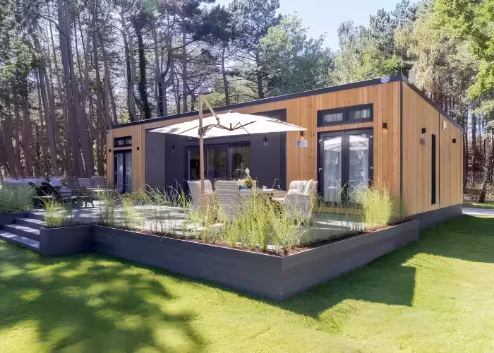 Provence Gaja – Moderne houten woning met terras, parasol en tuinmeubilair omgeven door gras en bomen.