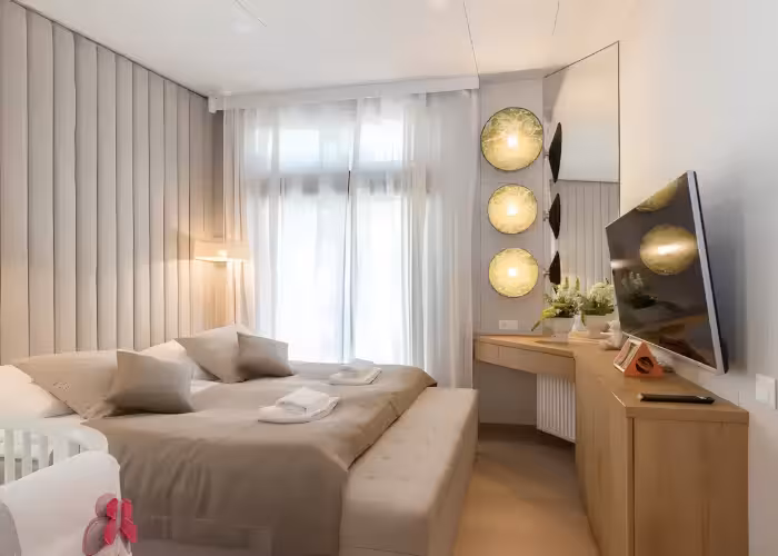 Provence Gaja – Slaapkamer met groot bed, gordijnen, wandlamp en televisie aan een houten meubel.