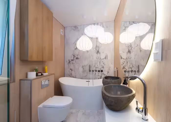 Provence Gaja – Moderne badkamer met vrijstaand wit bad, stenen wastafels, grote spiegel en houten kasten.
