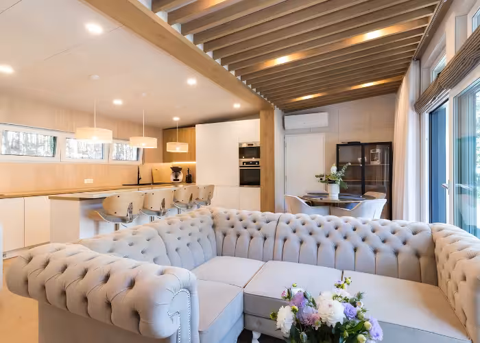 Provence Gaja – Lichte moderne woonkamer met een L-vormige gestoffeerde bank, open keuken en grote ramen.