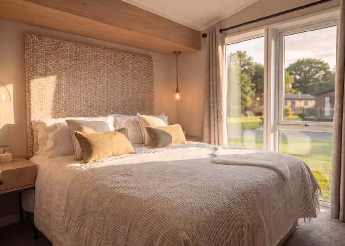 Davenport – Slaapkamer met een groot bed, beige dekbed en kussens naast een raam met uitzicht op groen.