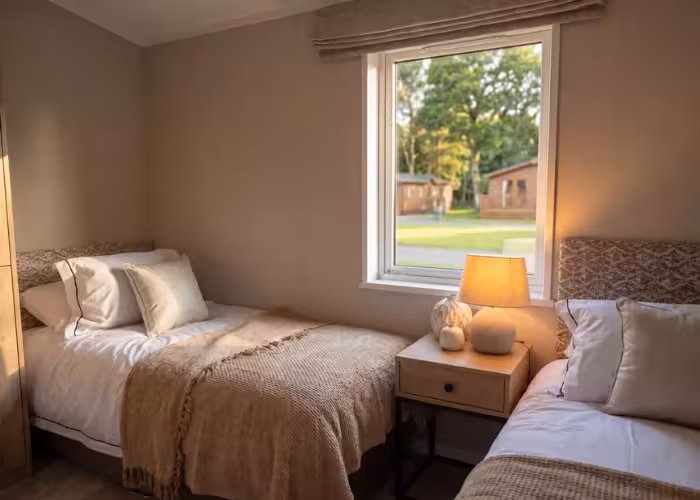 Davenport – Twee eenpersoonsbedden met witte kussens en beige dekens in een rustige kamer met raam.