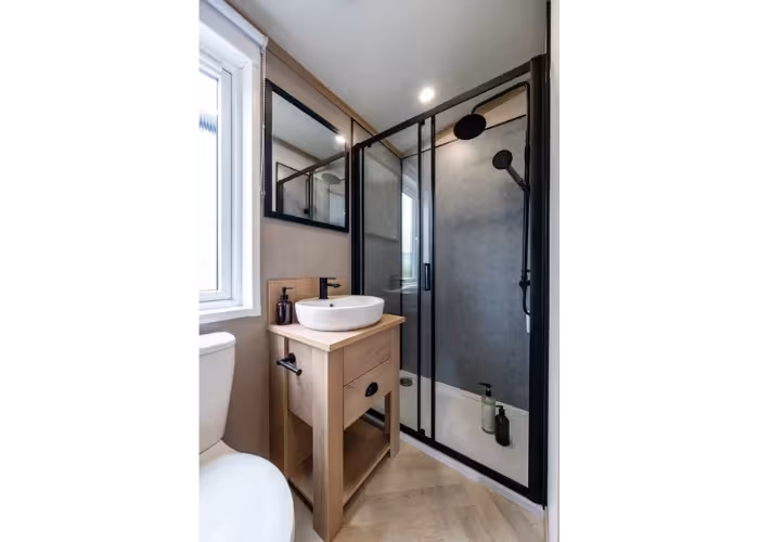 Davenport – Moderne badkamer met houten wastafelmeubel, rond wit waskom, zwarte douchecabine en toilet naast raam.