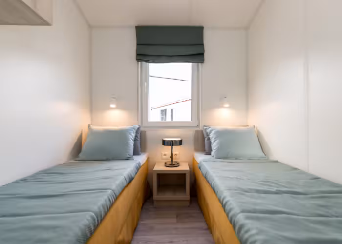 Ballum Terras – Twee eenpersoonsbedden met groene dekens en kussens gescheiden door een nachtkastje met lamp, raam erboven.