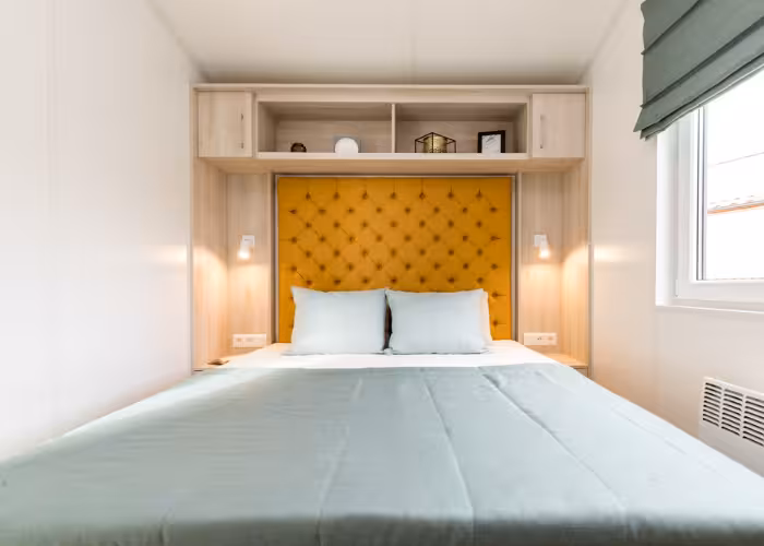 Ballum Terras – Slaapkamer met bed met geel gestoffeerd hoofdeinde en kast met planken rondom.