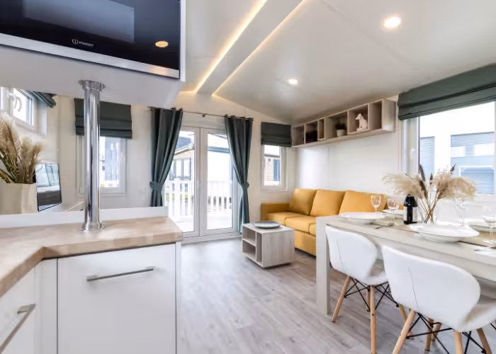 Ballum Terras – Moderne woonkamer met gele bank, eettafel met witte stoelen, en glazen deuren met groene gordijnen.