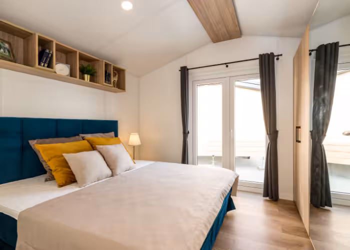 G-Spot – Slaapkamer met groot bed, gele en witte kussens, houten vloeren en een deur naar balkon.