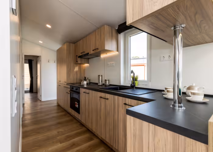 G-Spot – Moderne keuken met houtlook kasten, zwart werkblad en raam met uitzicht buiten.