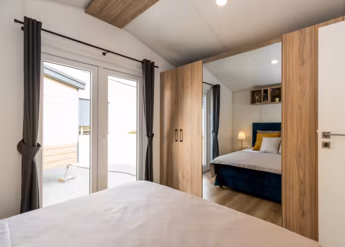 G-Spot – Slaapkamer met een bed, houten kast met spiegel en glasdeuren met gordijnen.