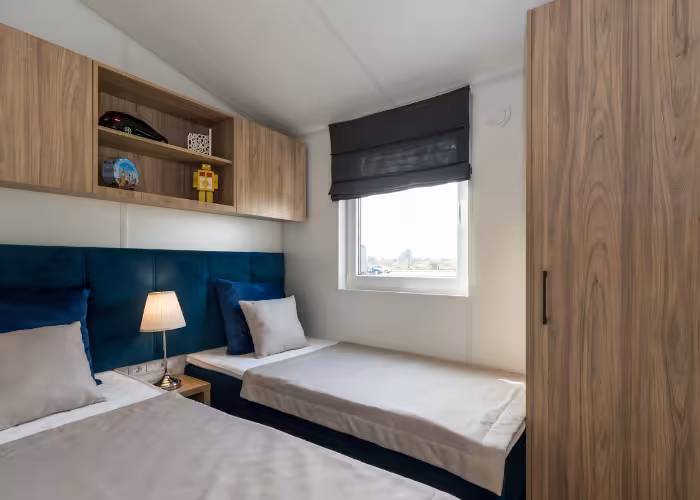 G-Spot – Slaapkamer met twee eenpersoonsbedden, blauw gestoffeerd hoofdeinde, nachtlamp en houten kasten.