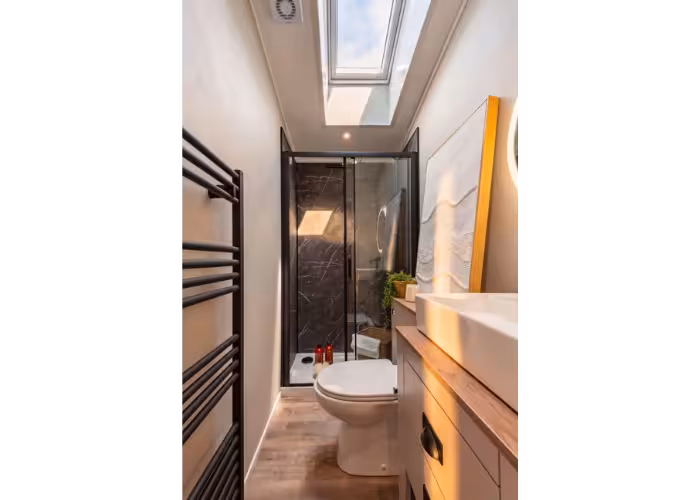 Lakewood – Moderne smalle badkamer met douche, toilet, wastafel, kast en een dakraam voor natuurlijk licht.