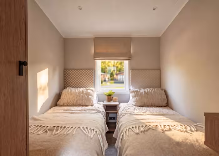 Lakewood – Twee eenpersoonsbedden met beige dekens en kussens in een kamer met raam in het midden.