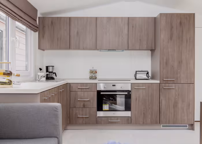Korfu – Moderne keuken met houten kasten, ingebouwde oven, koffiezetapparaat en broodrooster bij raam.