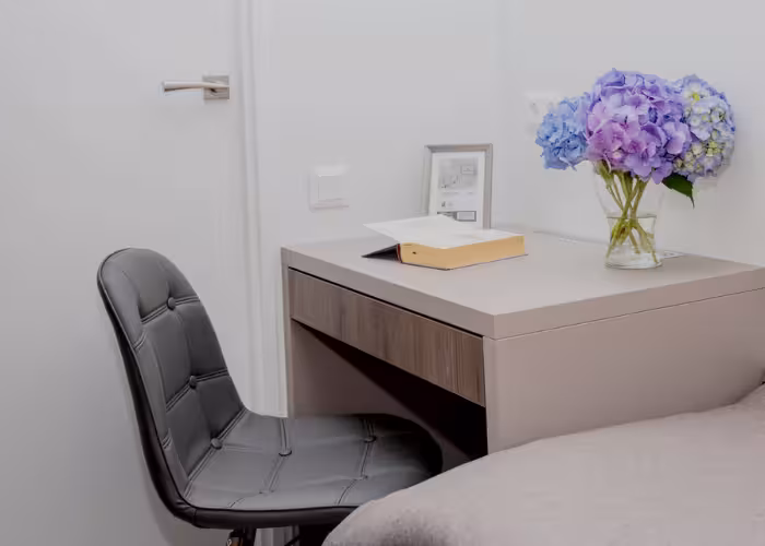 Korfu – Kleine schrijftafel met geopend boek en vaas met paarse bloemen naast een zwarte stoel.