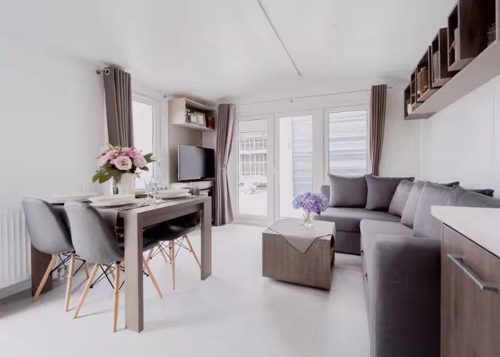 Korfu – Moderne woonkamer met grijze hoekbank, eettafel met stoelen en bloemen op tafel.