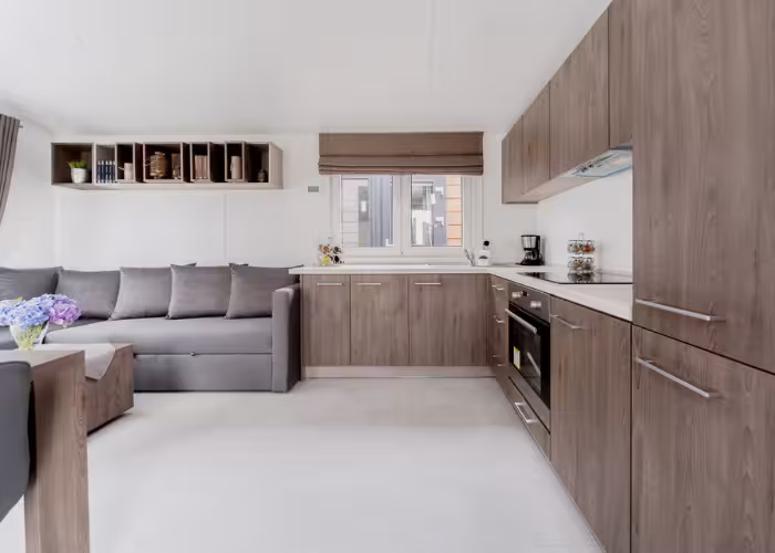 Korfu – Moderne keuken met houten kasten, grijze bank en raam met bruine jaloezieën.