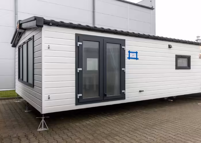 Texel – Witte woonunit met zwarte kozijnen en dubbele glazen deuren op betonnen vloer buiten.