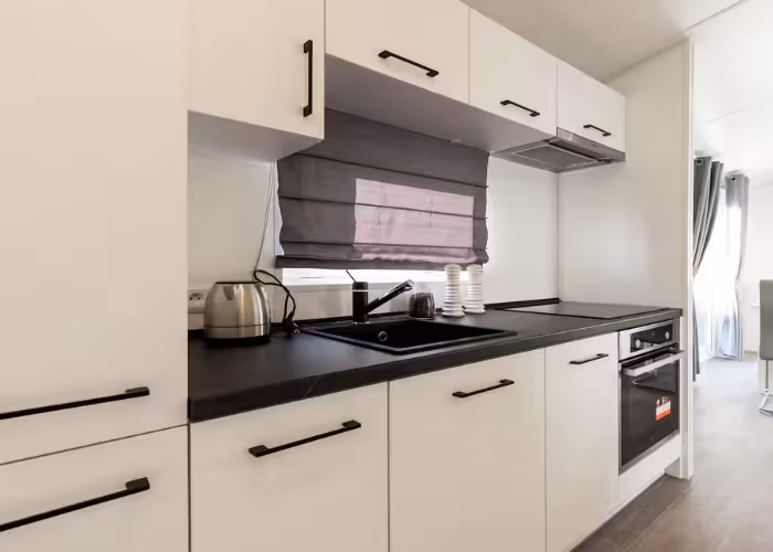 Texel – Moderne witte keuken met zwart werkblad, spoelbak, waterkoker en ingebouwde oven onder zwart rolluik.