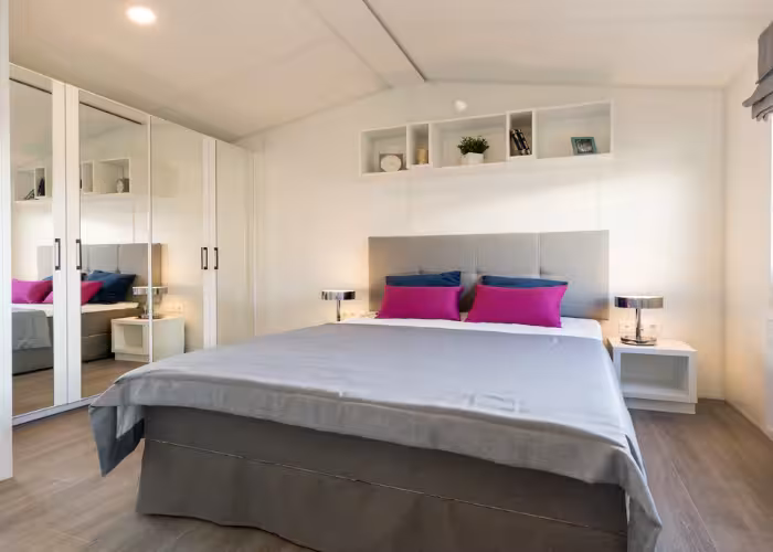 Texel – Slaapkamer met groot bed, paars en blauw beddengoed, witte kast met spiegels en minimalistisch interieur.