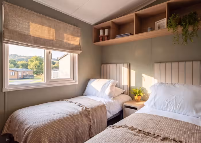 Arlington – Twee eenpersoonsbedden met witte kussens en beige dekens in een slaapkamer met raam en planken.