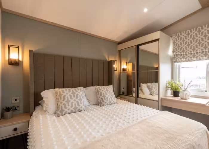 Harraway – Slaapkamer met groot bed, lichte decoratie, spiegelkasten en raam met planten op vensterbank.