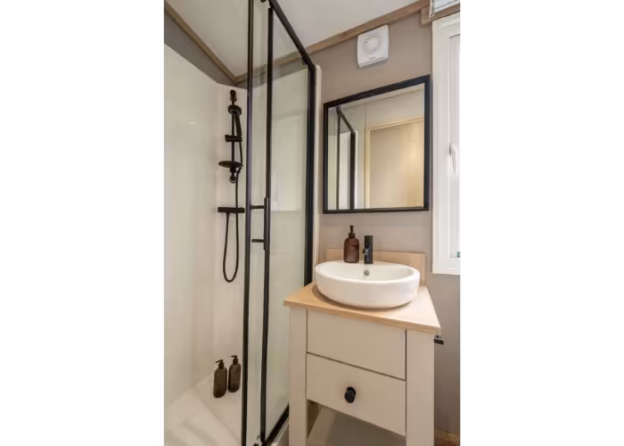 Harraway – Compacte badkamer met glazen douchecabine, ronde waskom op een houten meubel en wandspiegel.