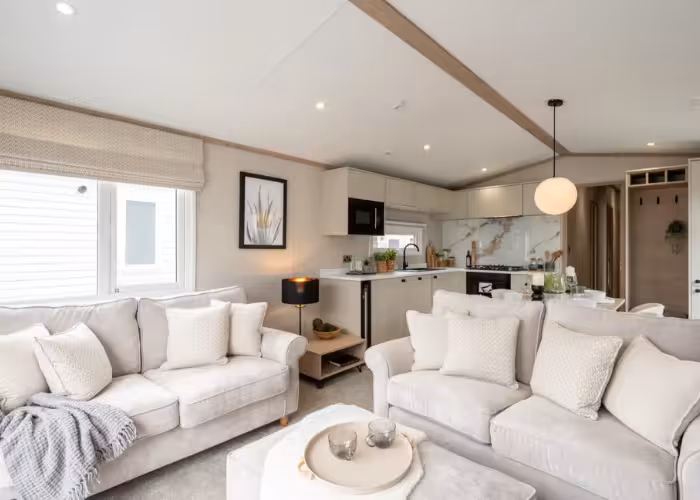 Harraway – Lichte woonkamer met twee beige banken, een salontafel en open keuken met moderne inrichting.